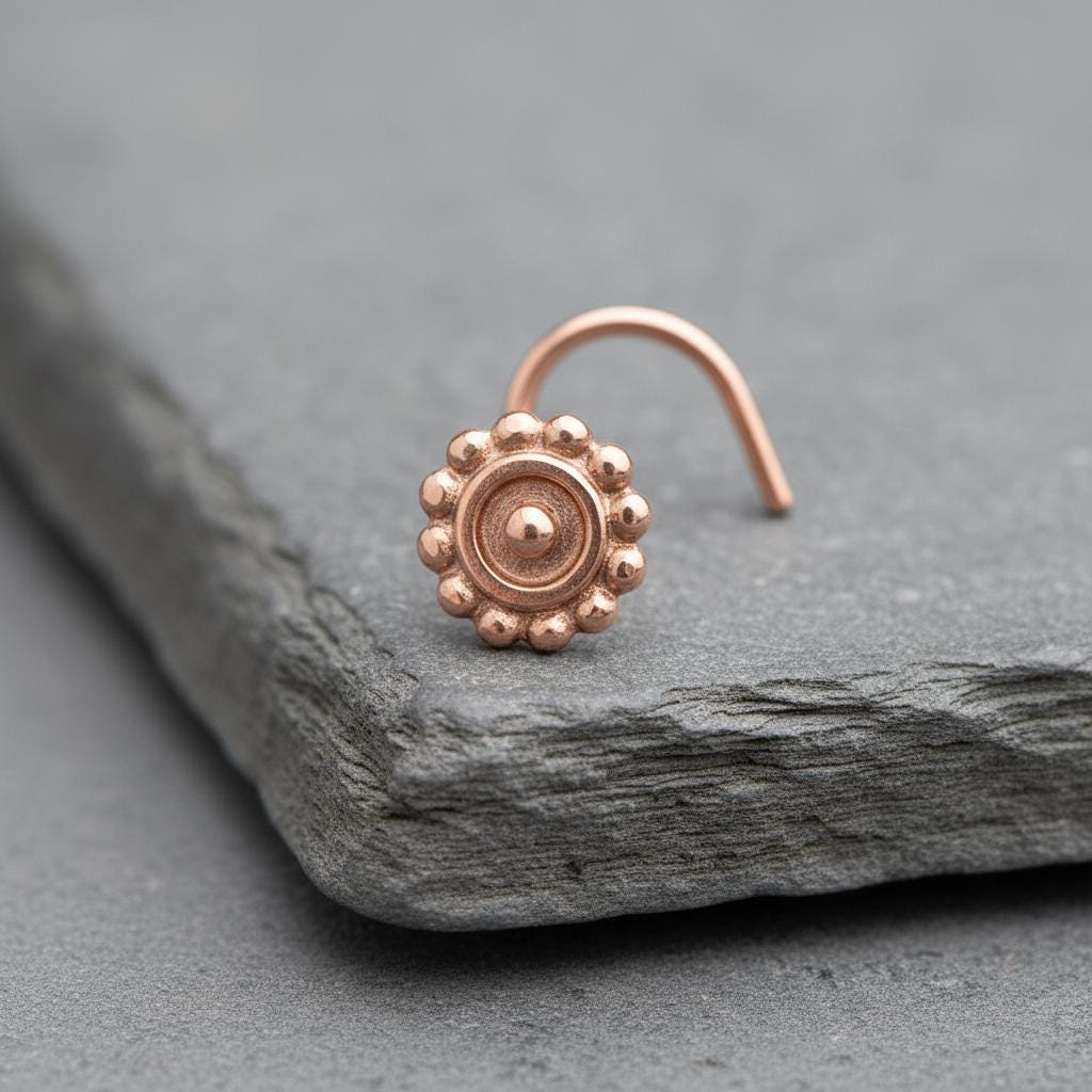 A copper-colored nose ring with a circular design sits on a gray surface.