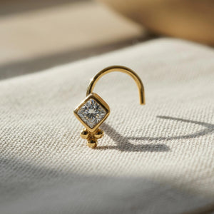 Diamond Nose Stud: A gold nose stud with a diamond-like center stone is displayed on a white fabric surface.