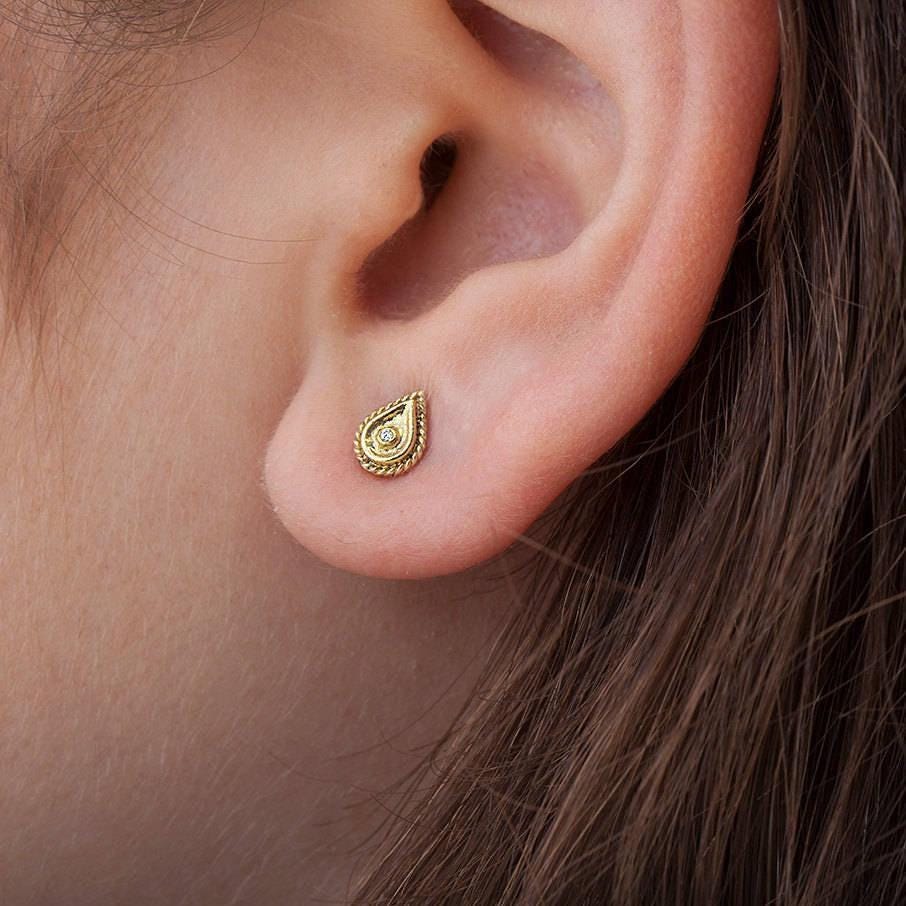 A close-up view of a person's ear, showing a small gold earring with a decorative design.
