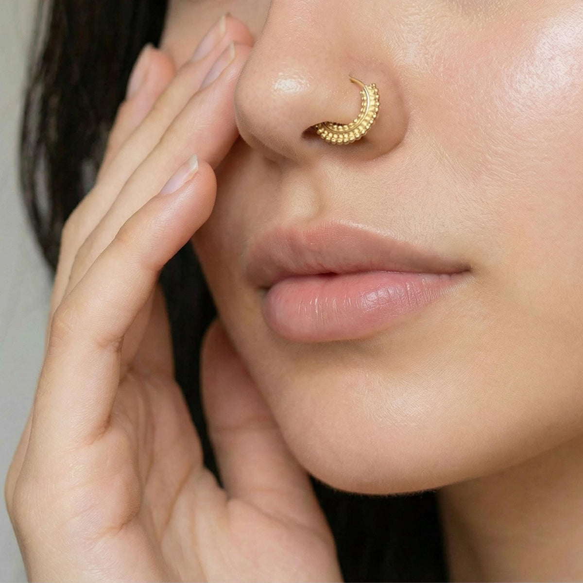 A close-up of a person's face, focusing on their nose and fingers, with a gold nose ring visible.