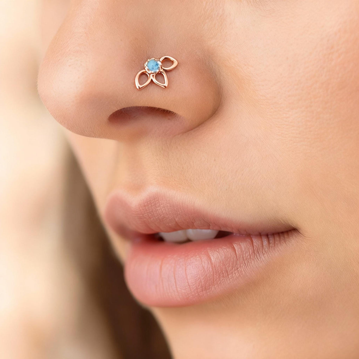 A close-up of a person's nose and lips, with a delicate nose ring featuring a blue gemstone.