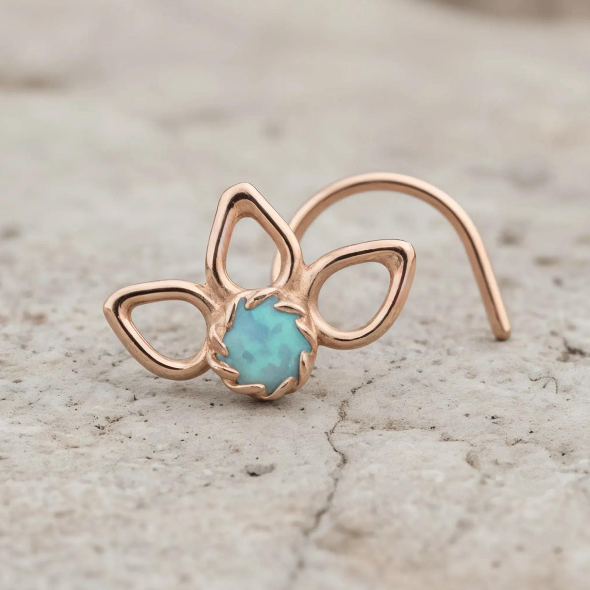 A rose gold nose ring with a blue stone in the center, resting on a rock surface.