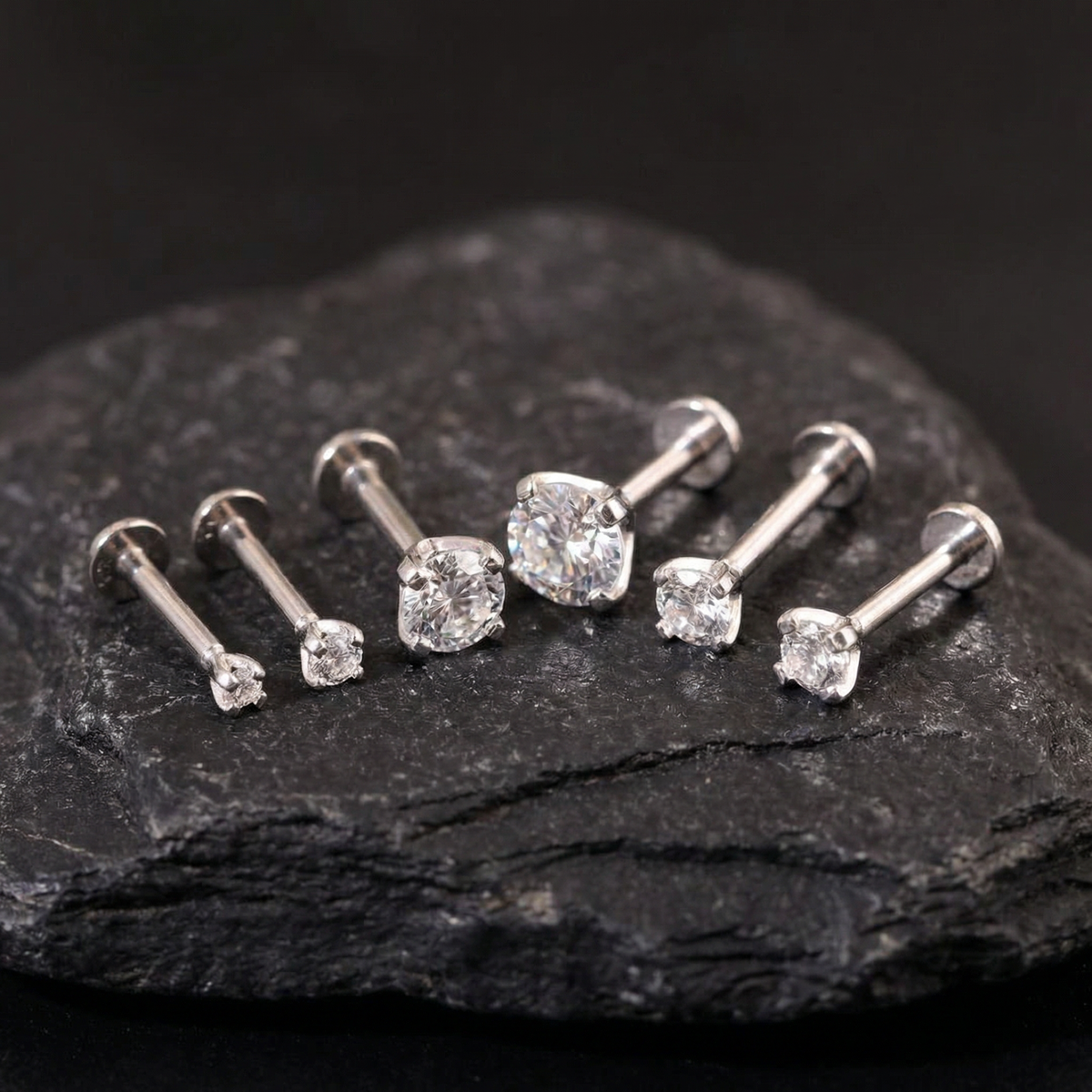 A collection of six diamond-encrusted earrings is displayed on a dark surface, with the largest earring positioned centrally and the others surrounding it.