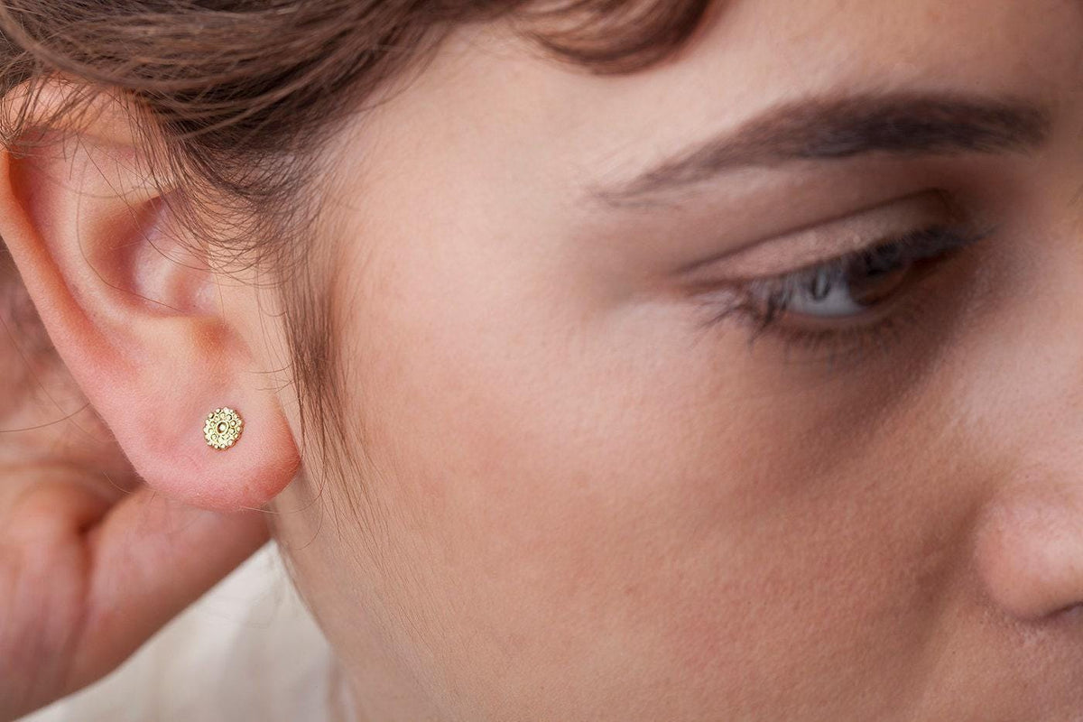 A close-up of a person's ear with a small gold earring in it.
