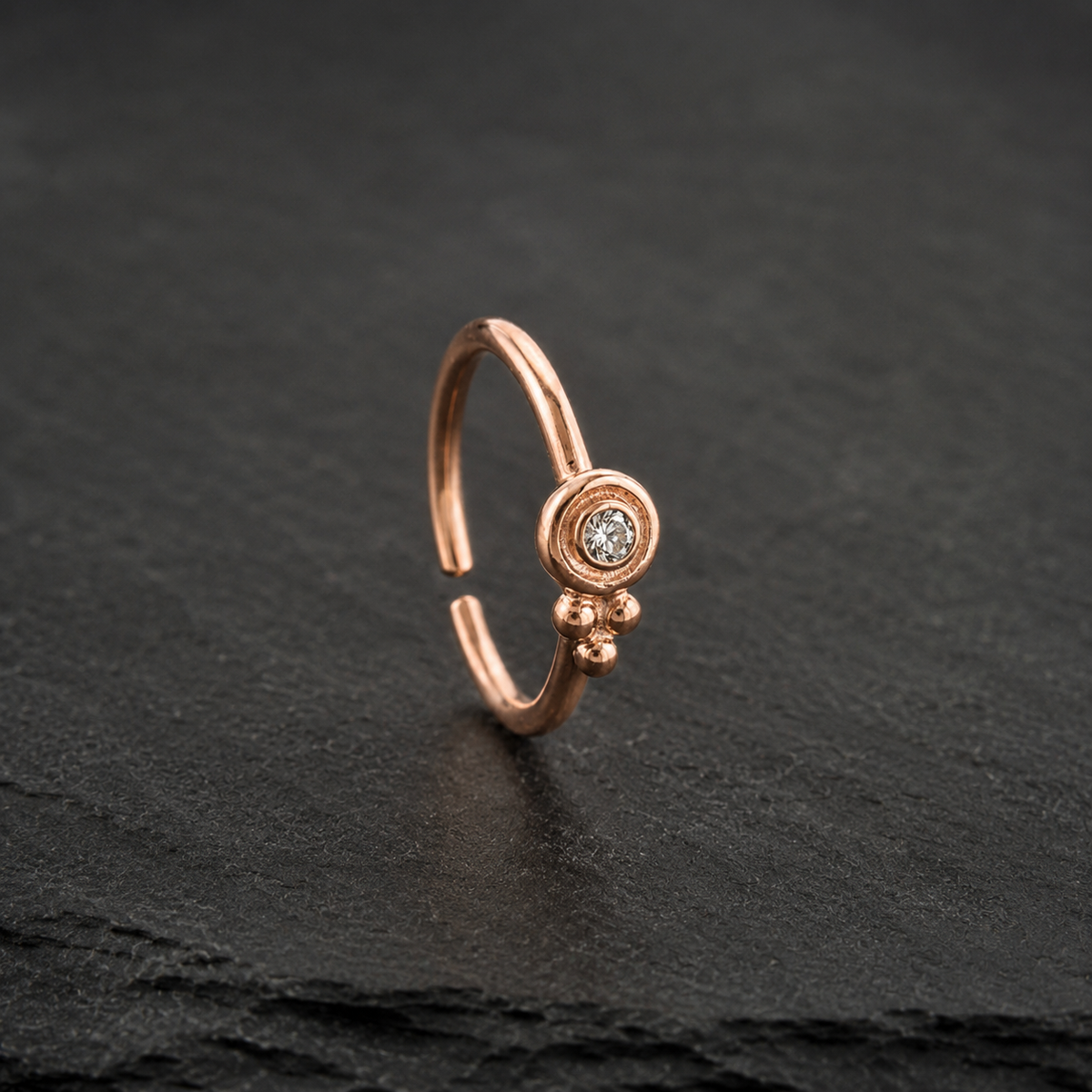A single, ornate gold-colored nose ring with a small diamond in the center, resting on a dark surface.