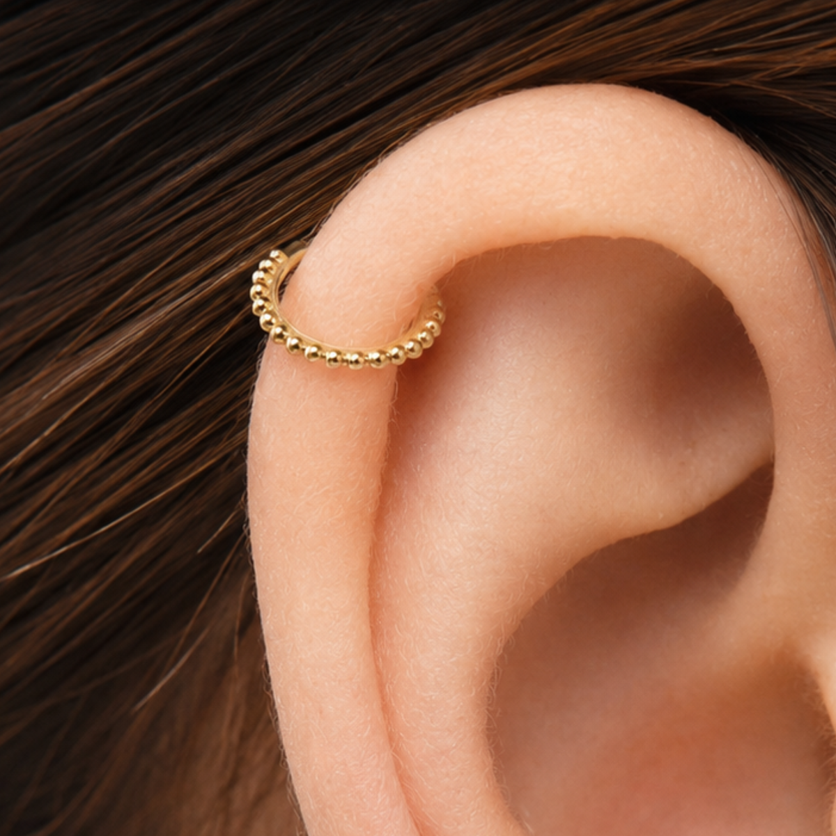 A gold-colored earring with a small ball-shaped design is visible in the image.