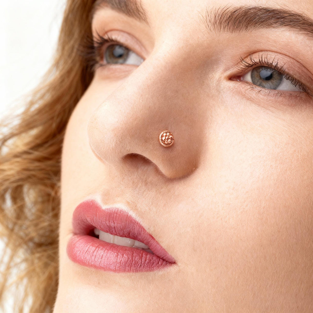 A close-up of a woman's face, focusing on her nose and lips. She has long, wavy hair and is wearing a nose ring.