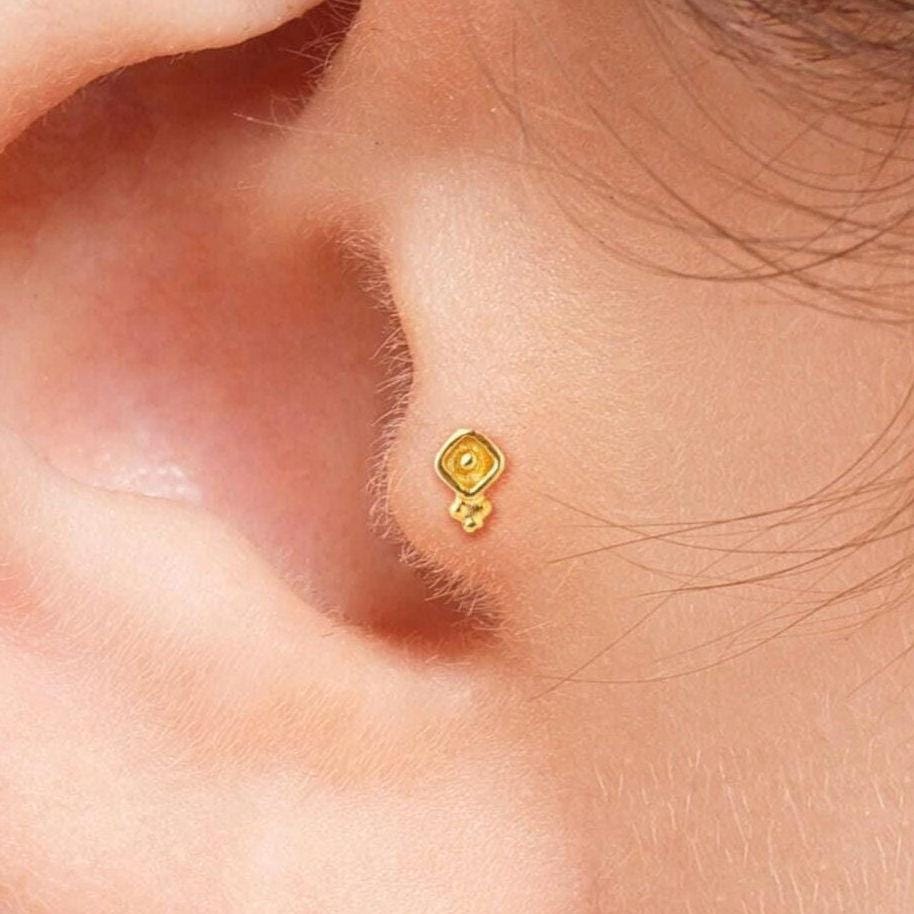 Boho 14k Gold Tragus Stud: A close-up view of a person's ear, showing a gold earring or stud in the earlobe.