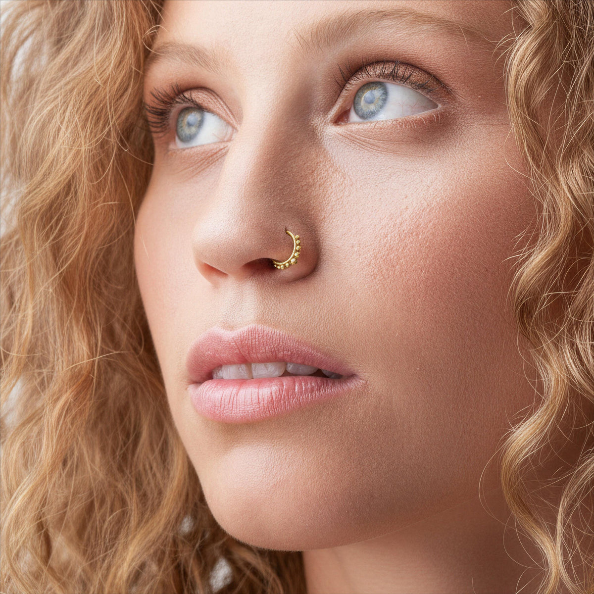 A close-up portrait of a woman with curly blonde hair, looking pensively to the side with a serious expression.