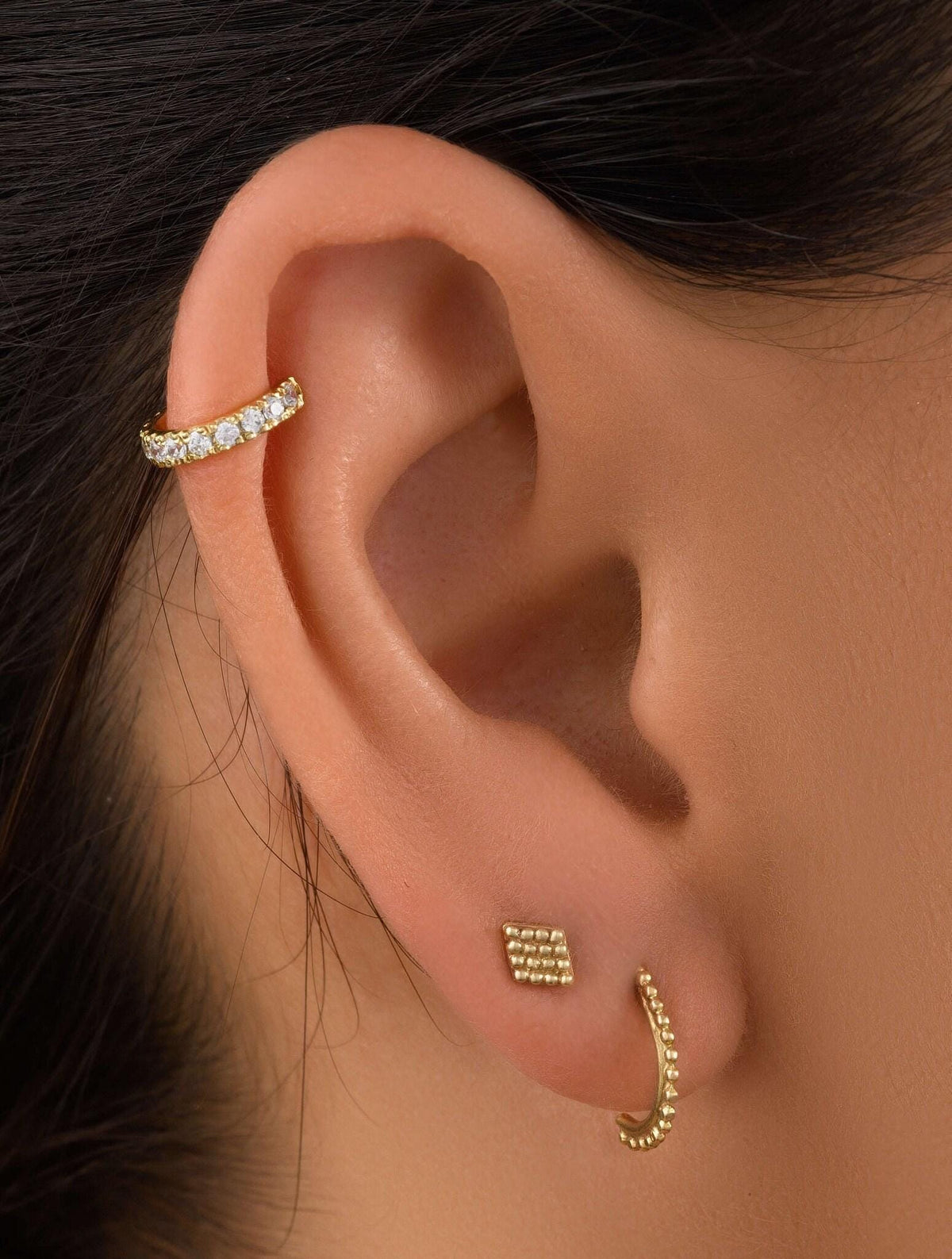 A close-up view of a person's ear adorned with two gold earrings, one of which is a small hoop earring and the other a larger earring with a diamond-like stone.
