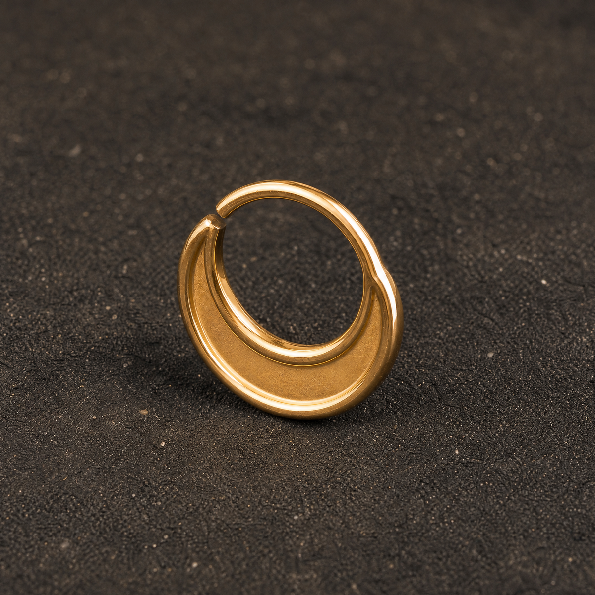 A gold-colored ring or earring is resting on a dark surface.