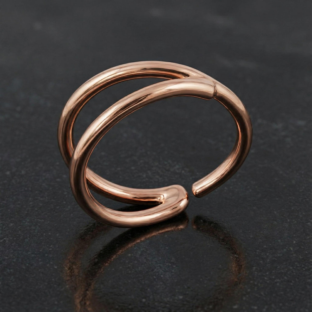 A shiny, metallic ring with a unique, twisted design sits on a dark surface.