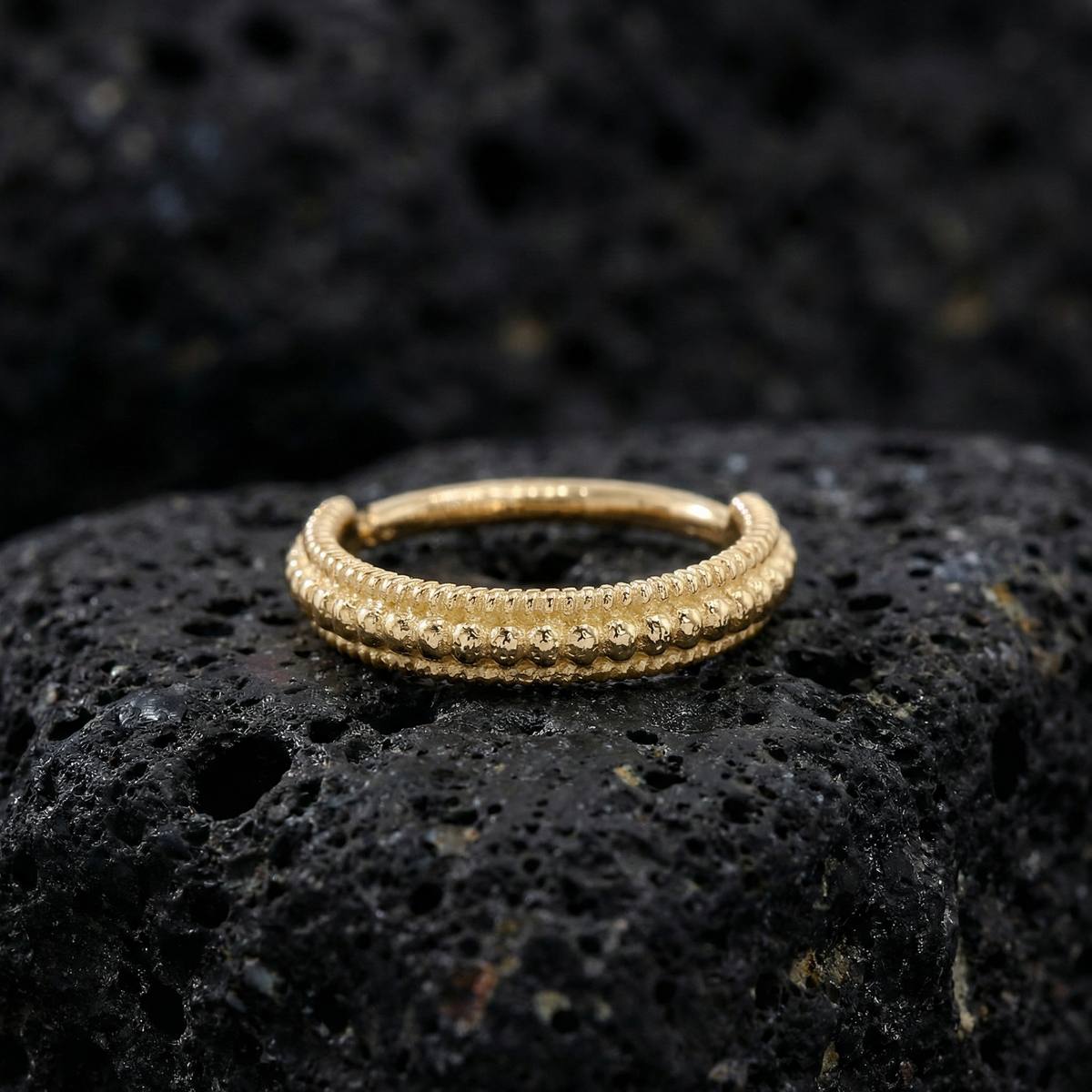 A gold-colored ring with a decorative band sits on a dark, textured surface.