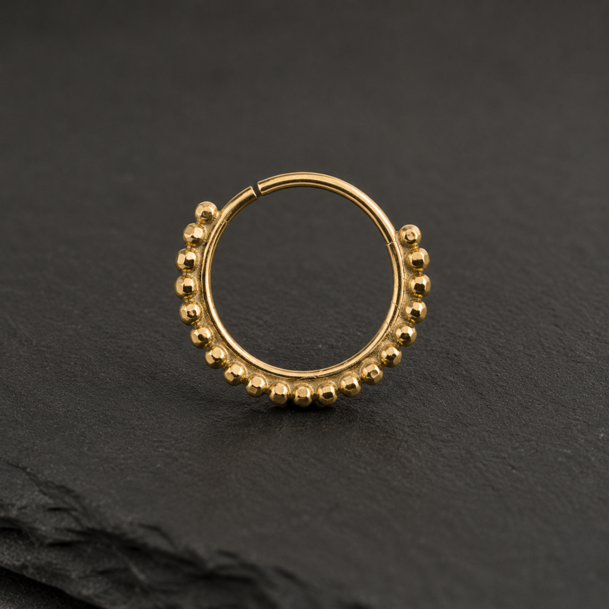 A gold-colored metal ring with a row of small, round beads or balls adorning the surface.