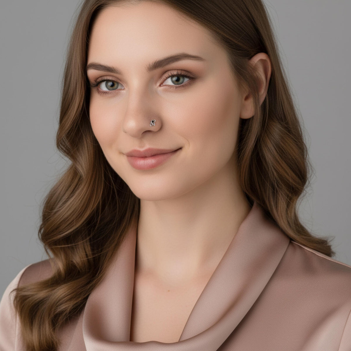 A portrait of a woman with long, wavy brown hair and a nose piercing, wearing a pink blouse.