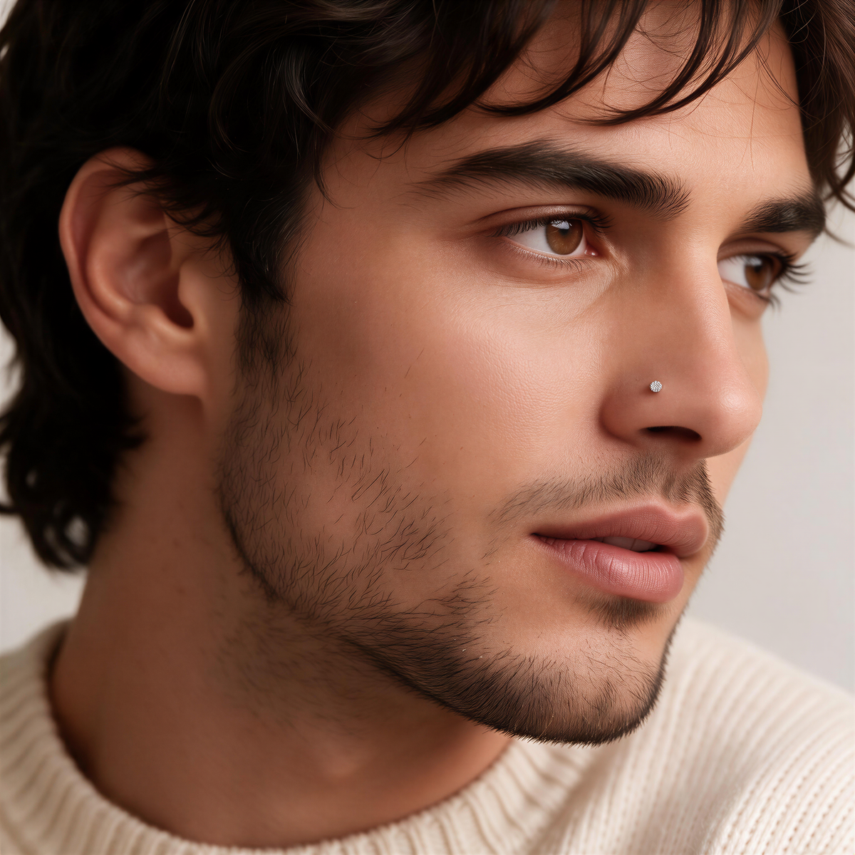 A close-up portrait of a man with dark hair and a beard, wearing a white sweater.