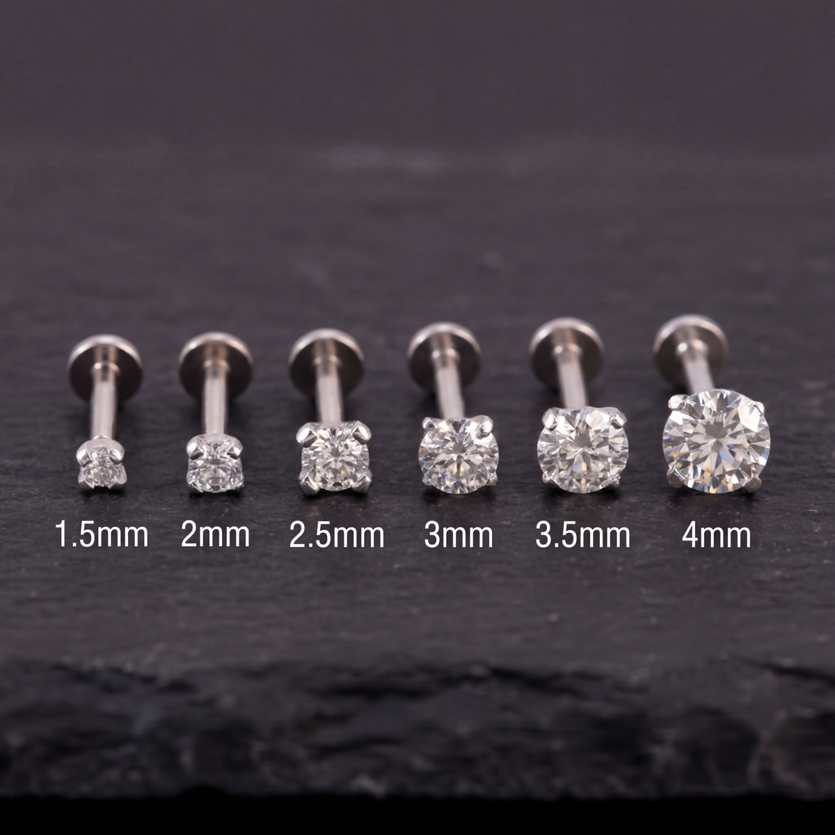 A collection of six diamond-encrusted piercings, each with a different size ranging from 1.5mm to 4mm, arranged in a row on a dark surface.