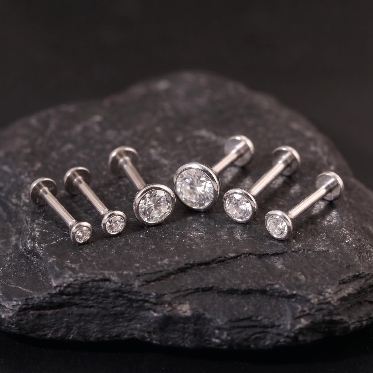 A collection of six silver-colored earrings with round stones, arranged on a dark surface.