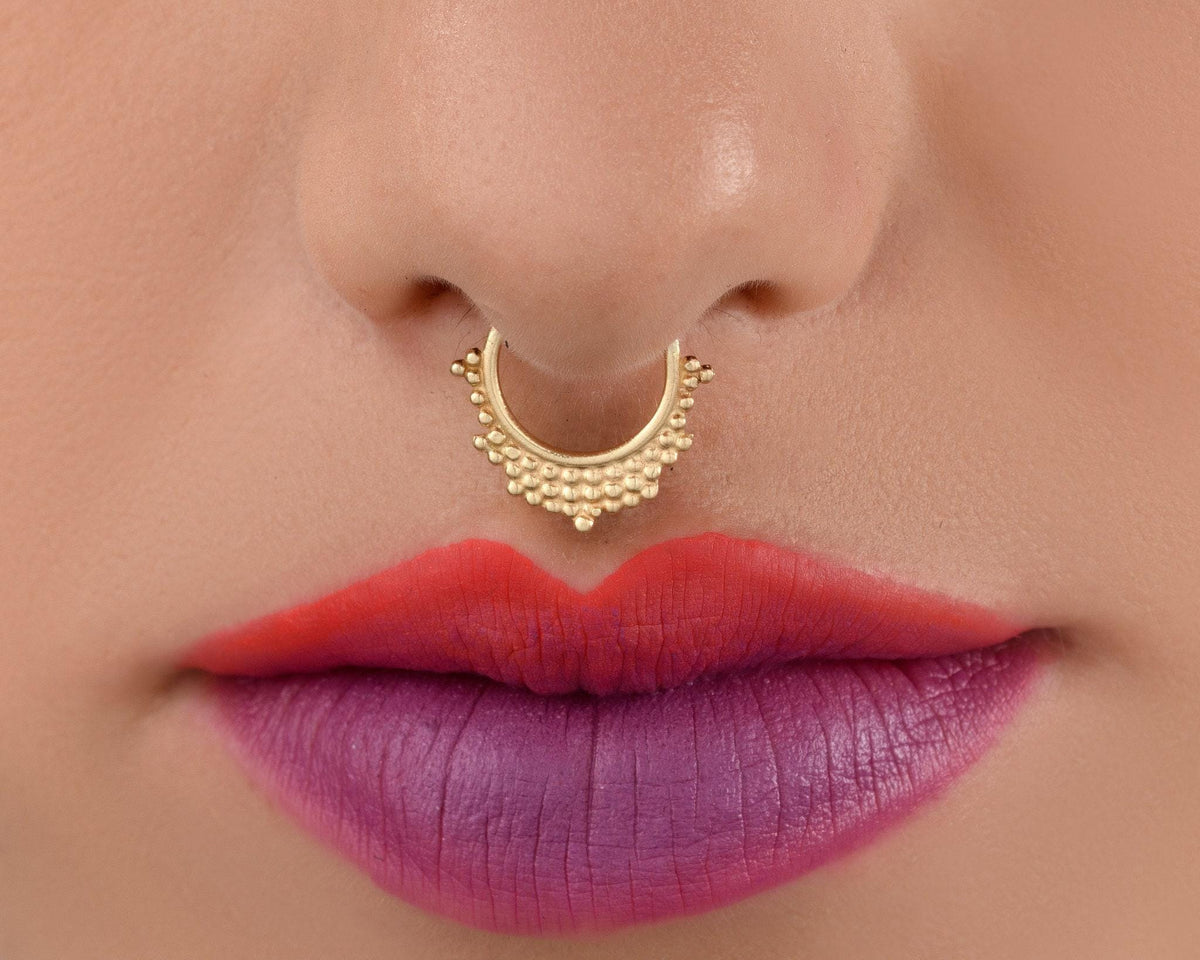 A close-up of a person's lips with a gold nose ring and red lipstick.