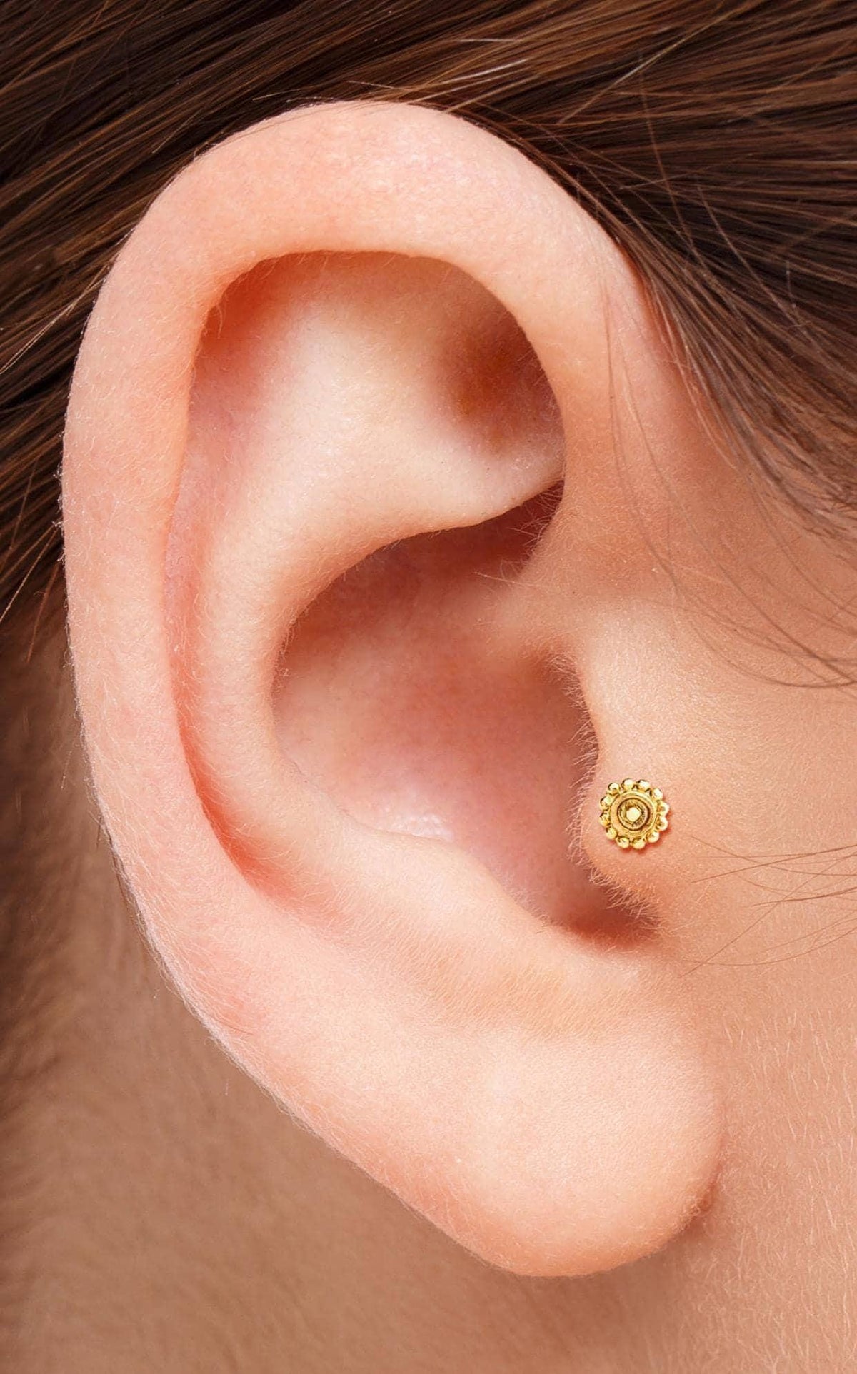 A close-up view of a person's ear, showing a small gold earring in the earlobe.