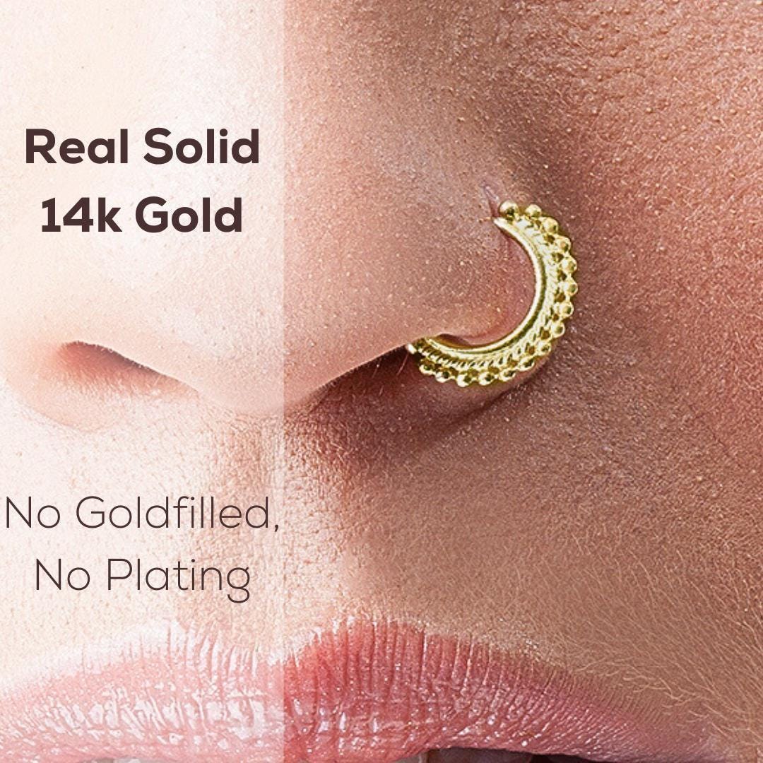 a close-up of a person's nose with a 14k gold hoop earring inserted into it.