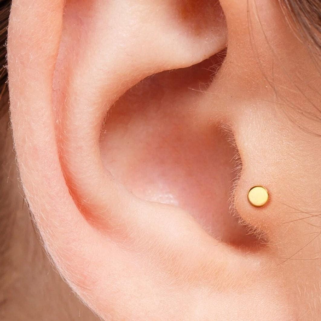 A close-up view of a person's ear, showing a small gold earring in the earlobe.