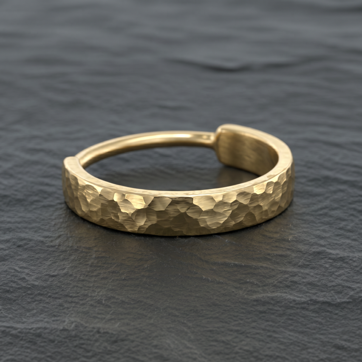 A close-up image of a gold ring with a textured surface, resting on a dark surface.