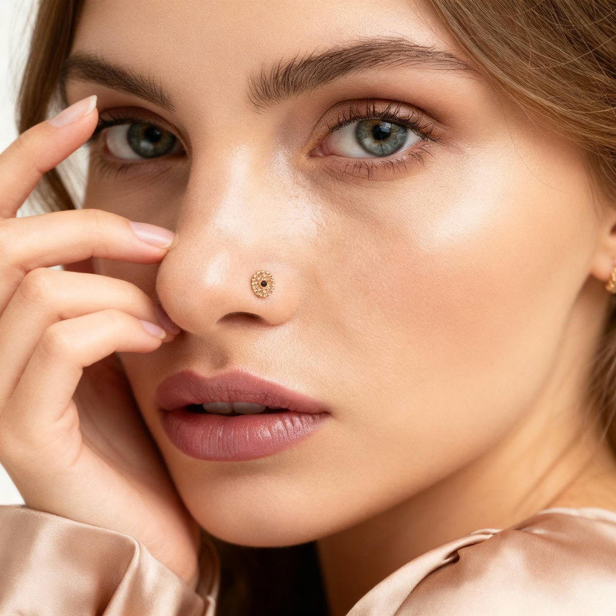 A close-up portrait of a woman with her hand on her nose, wearing a gold nose ring.