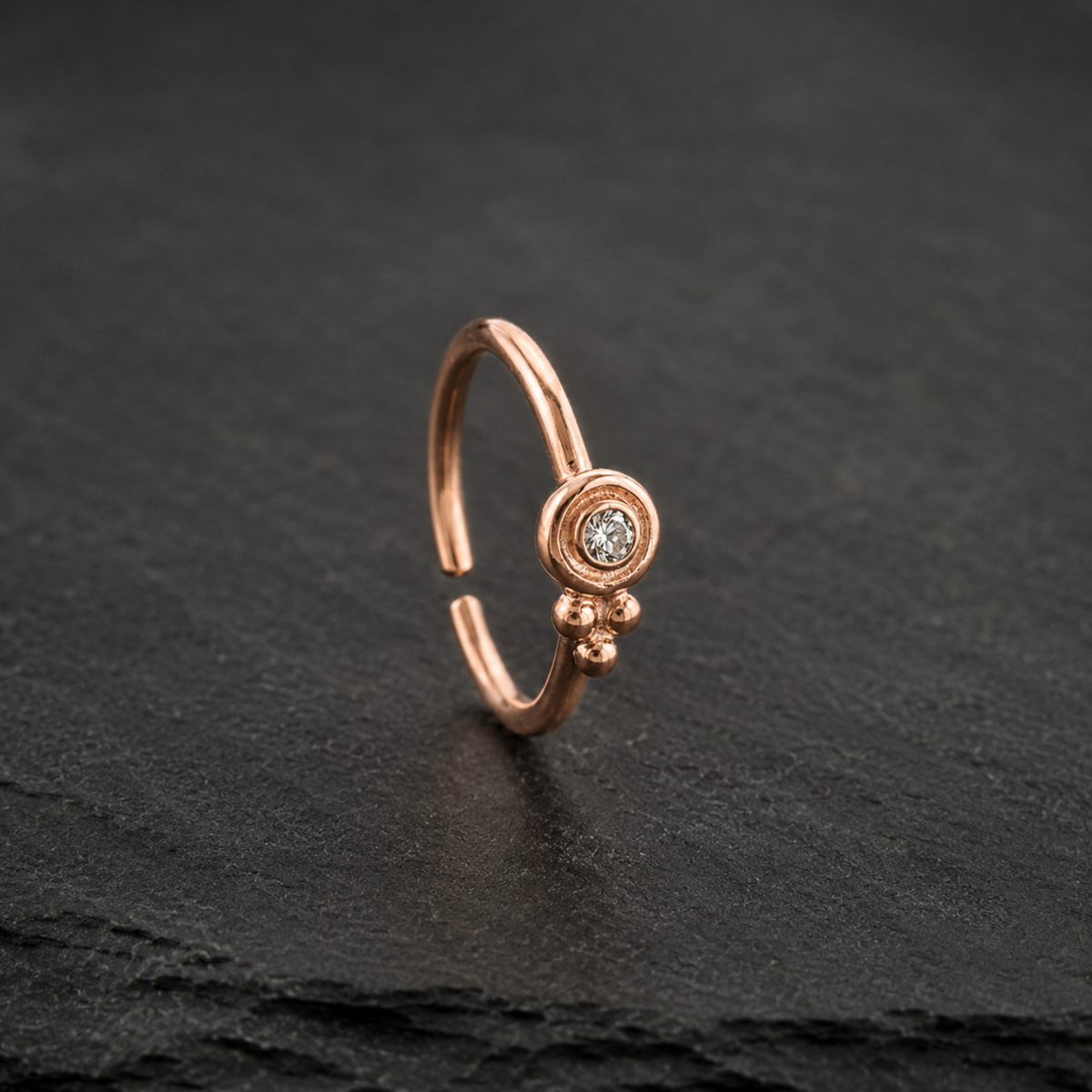 A single, ornate gold-colored nose ring with a small diamond in the center, resting on a dark surface.