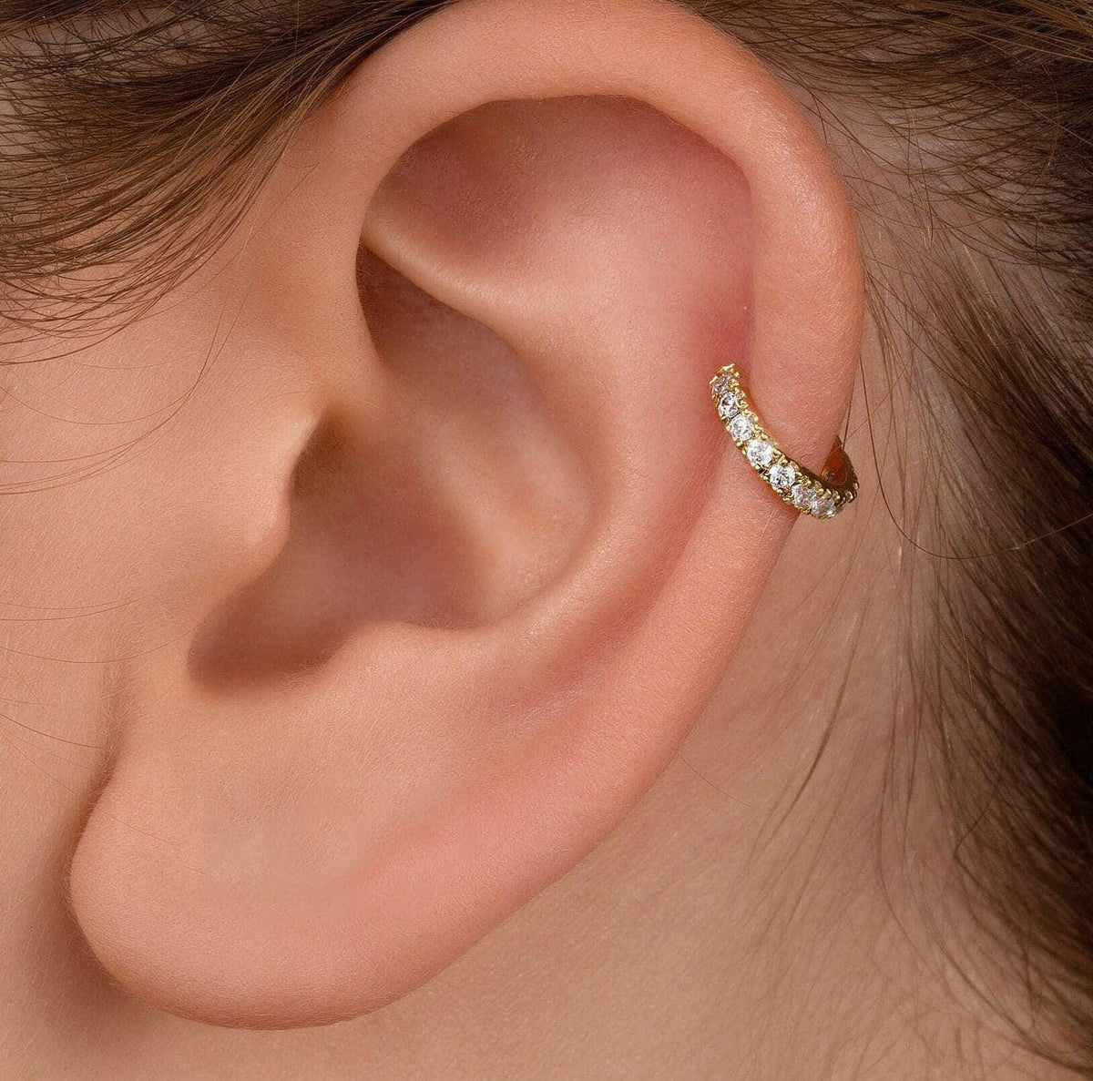 A close-up view of a person's ear, showing a gold earring with small diamonds.