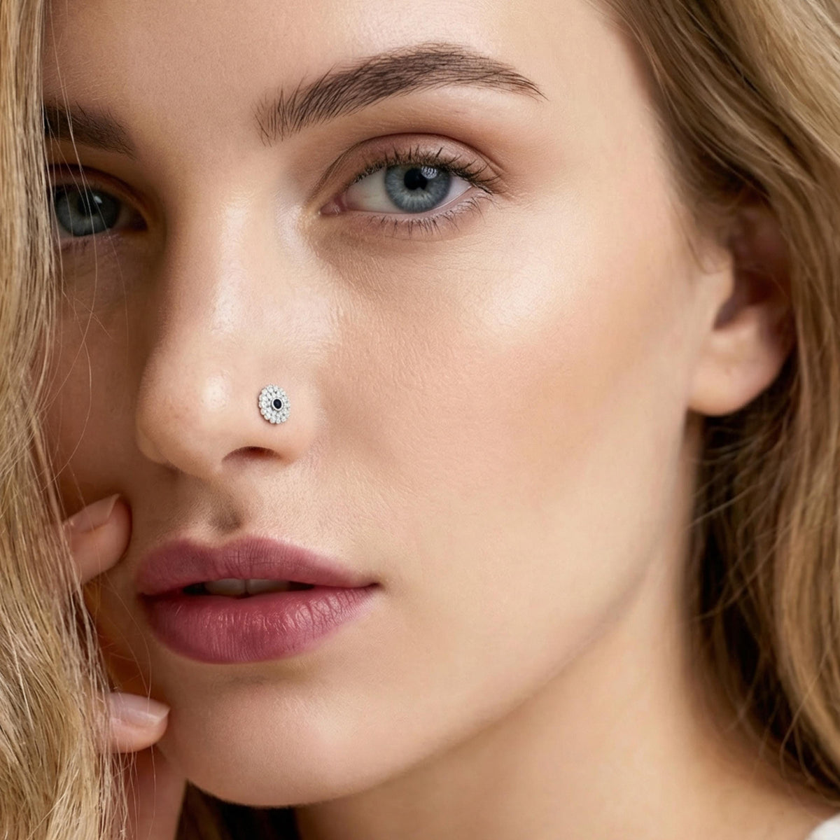 A close-up portrait of a woman with blonde hair and a nose piercing, looking directly at the camera with a thoughtful expression.