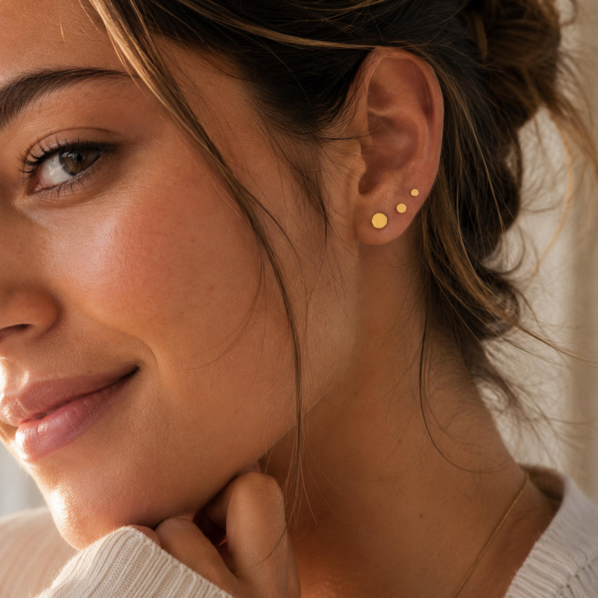 A close-up of a woman's face, focusing on her earrings and the side of her face.