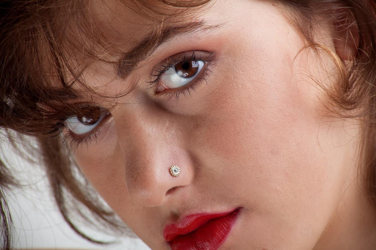A close-up portrait of a woman with brown hair and red lipstick, looking directly at the camera with a serious expression.