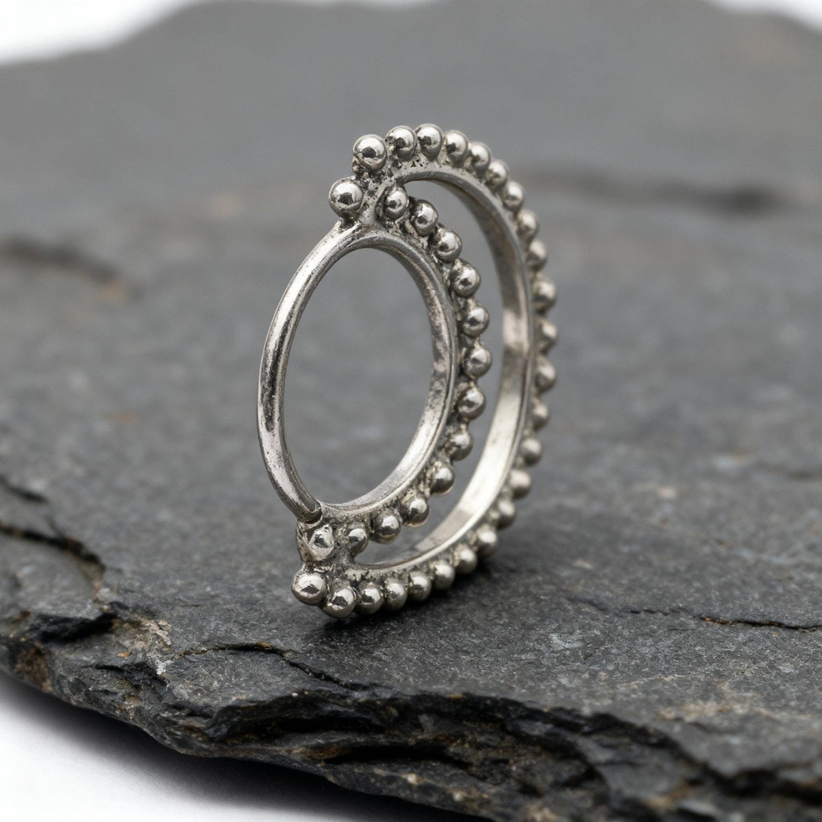 A silver ring with a decorative design sits on a gray rock.