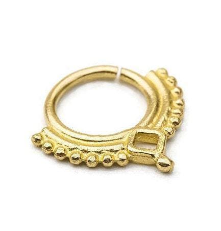 A gold-colored metal ring with a decorative design, featuring a square-shaped element and a row of small, round beads or stones along the edge.