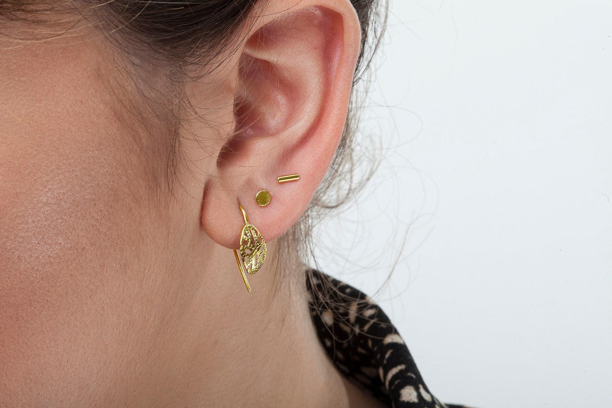 A close-up view of a person's ear adorned with two gold earrings, one of which has a leaf-like design.