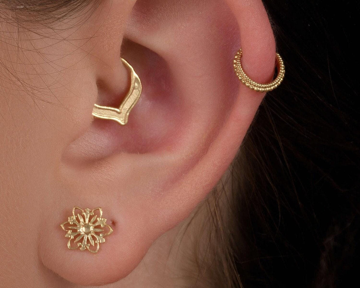 Whale Tail Daith Ring: A close-up of a person's ear adorned with two gold earrings, one of which is a hoop earring and the other a stud.