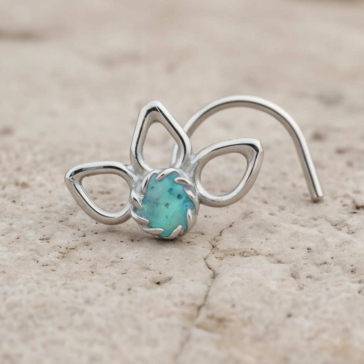 A silver nose ring with a turquoise stone is resting on a rock surface.
