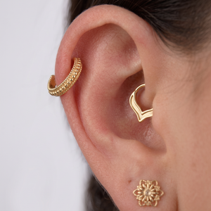 A close-up view of a person's ear adorned with two gold earrings, one of which is a hoop earring and the other a stud earring.