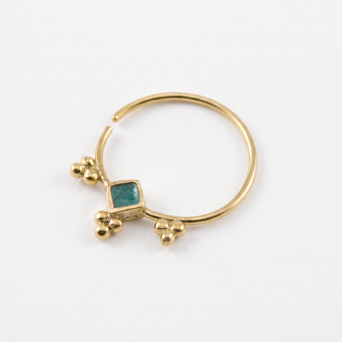 A gold-colored nose ring with a square gemstone in the center.