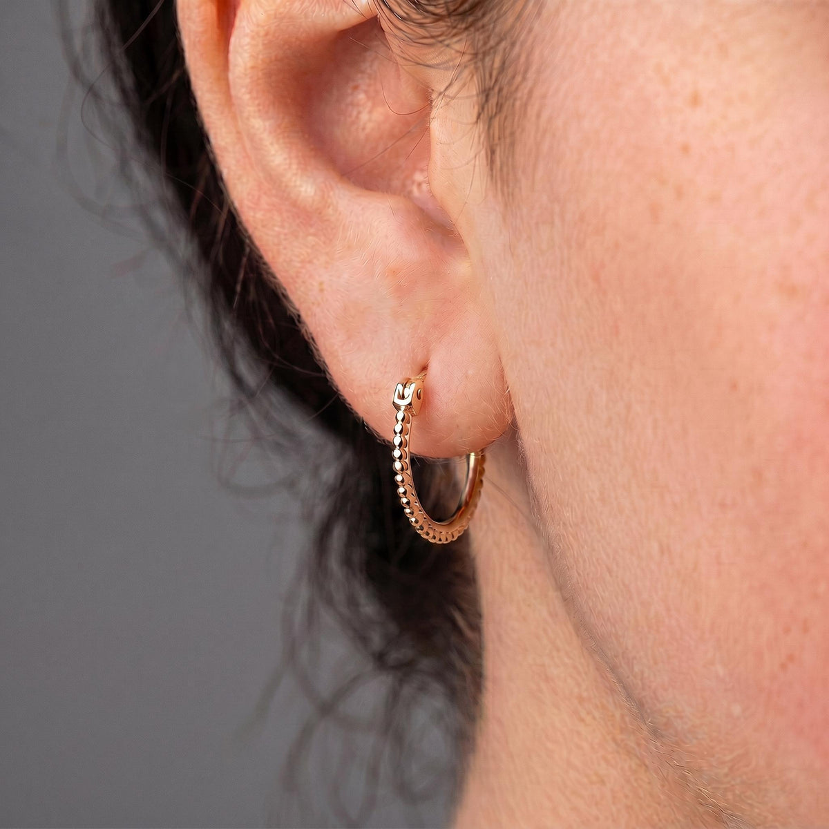 A close-up view of a person's ear adorned with a gold hoop earring.