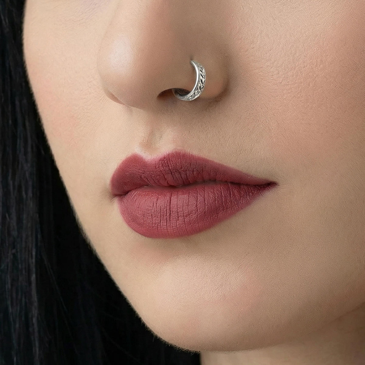 A close-up of a woman's face, focusing on her lips and nose. She has dark hair and is wearing a silver nose ring.