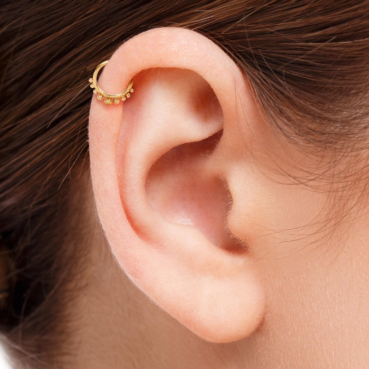 Helix Hoop Earring: A close-up view of a person's ear with a gold-colored earring in the earlobe.
