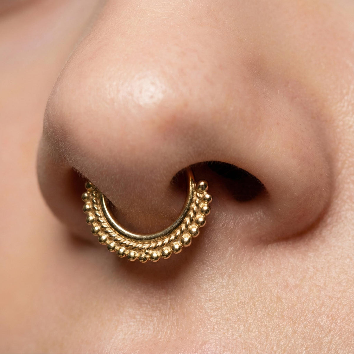 A close-up of a person's nose with a gold-colored nose ring featuring a decorative design.