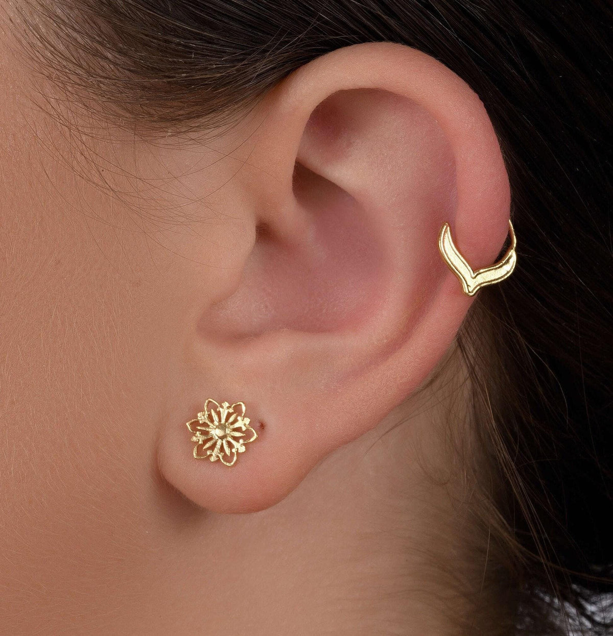 a close-up view of a person's ear adorned with two gold earrings.