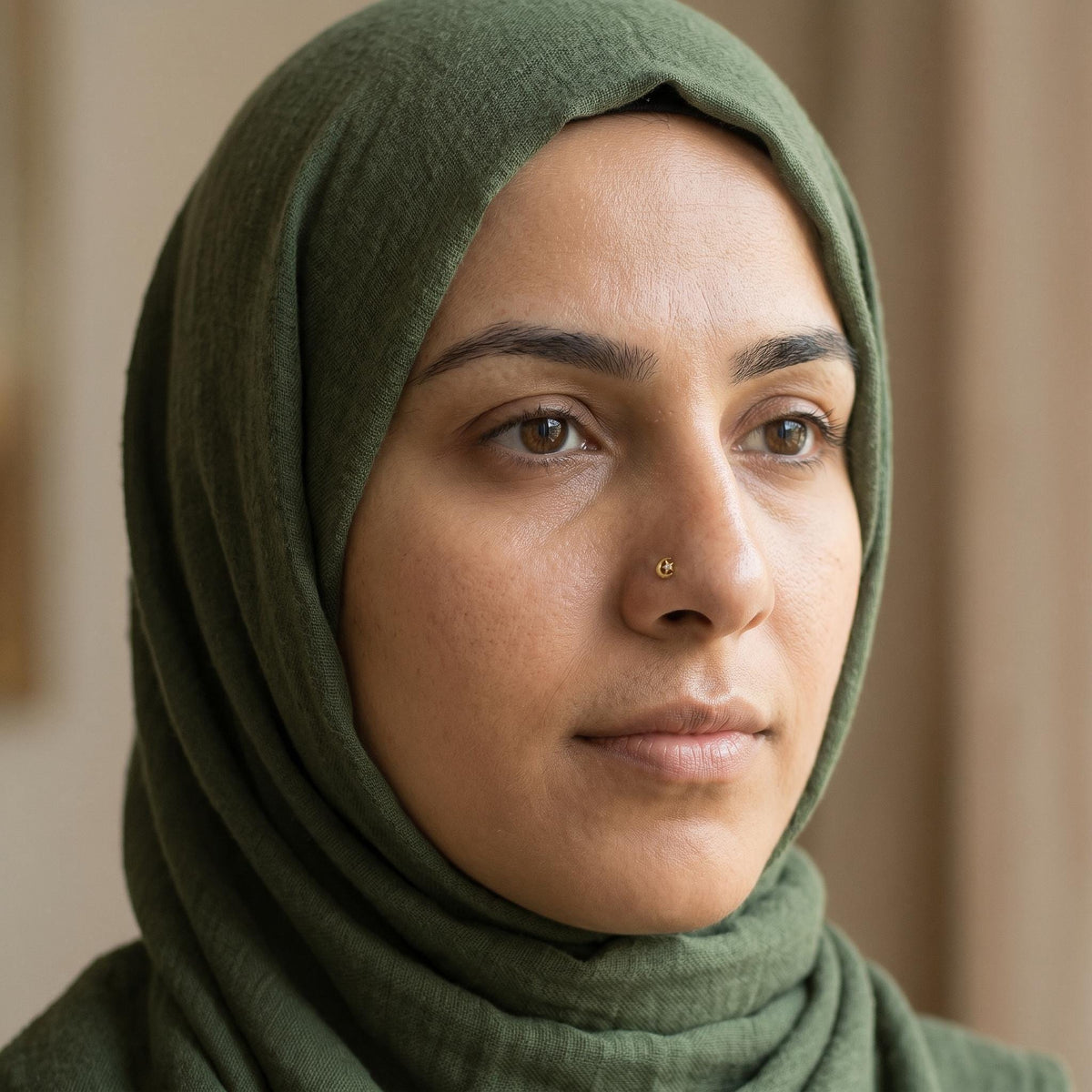A close-up portrait of a woman wearing a green hijab, with a neutral expression and a neutral gaze.
