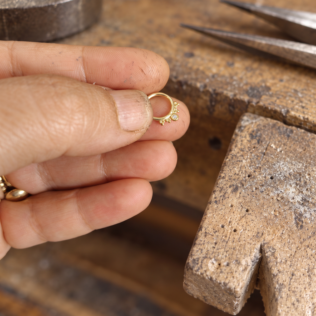 A hand holding a small gold ring with a decorative design on it.