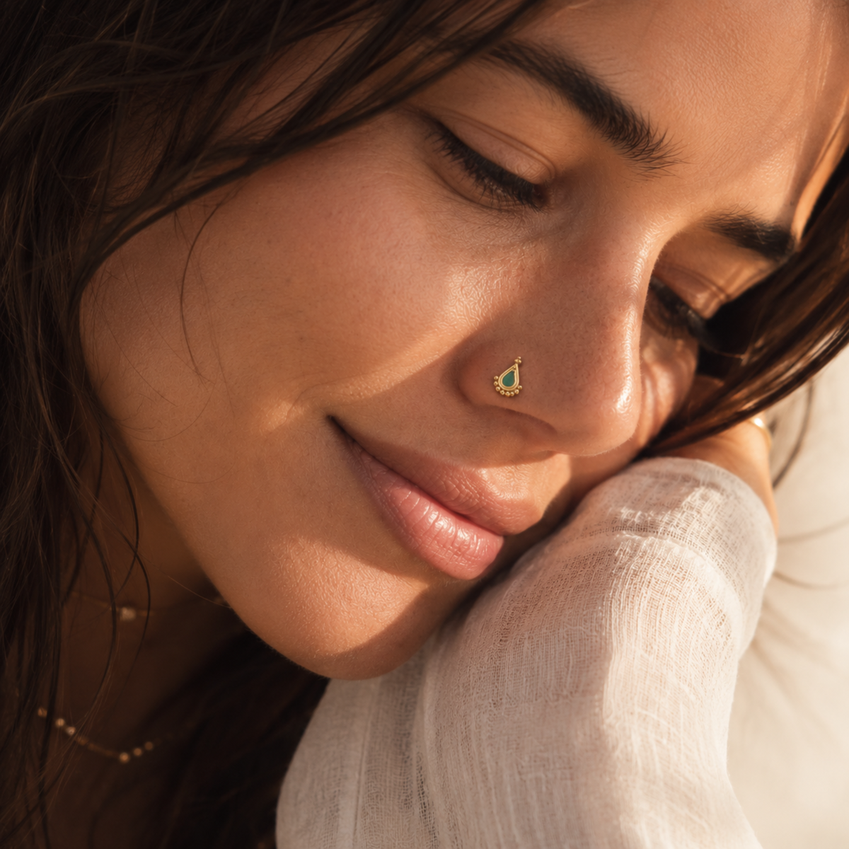 A close-up of a woman's face, with her eyes closed and a nose stud visible.