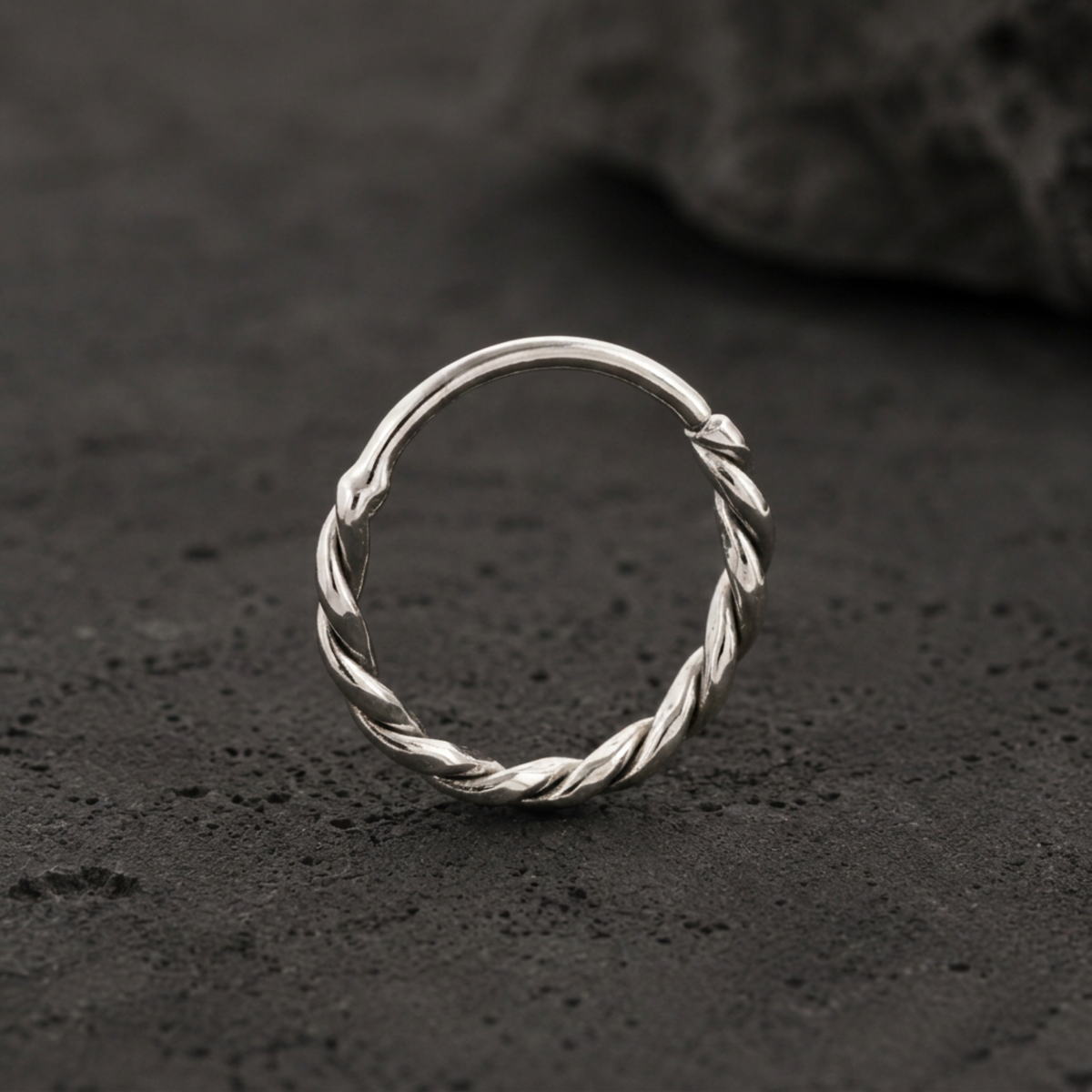 A silver ring with a twisted design sits on a dark surface.