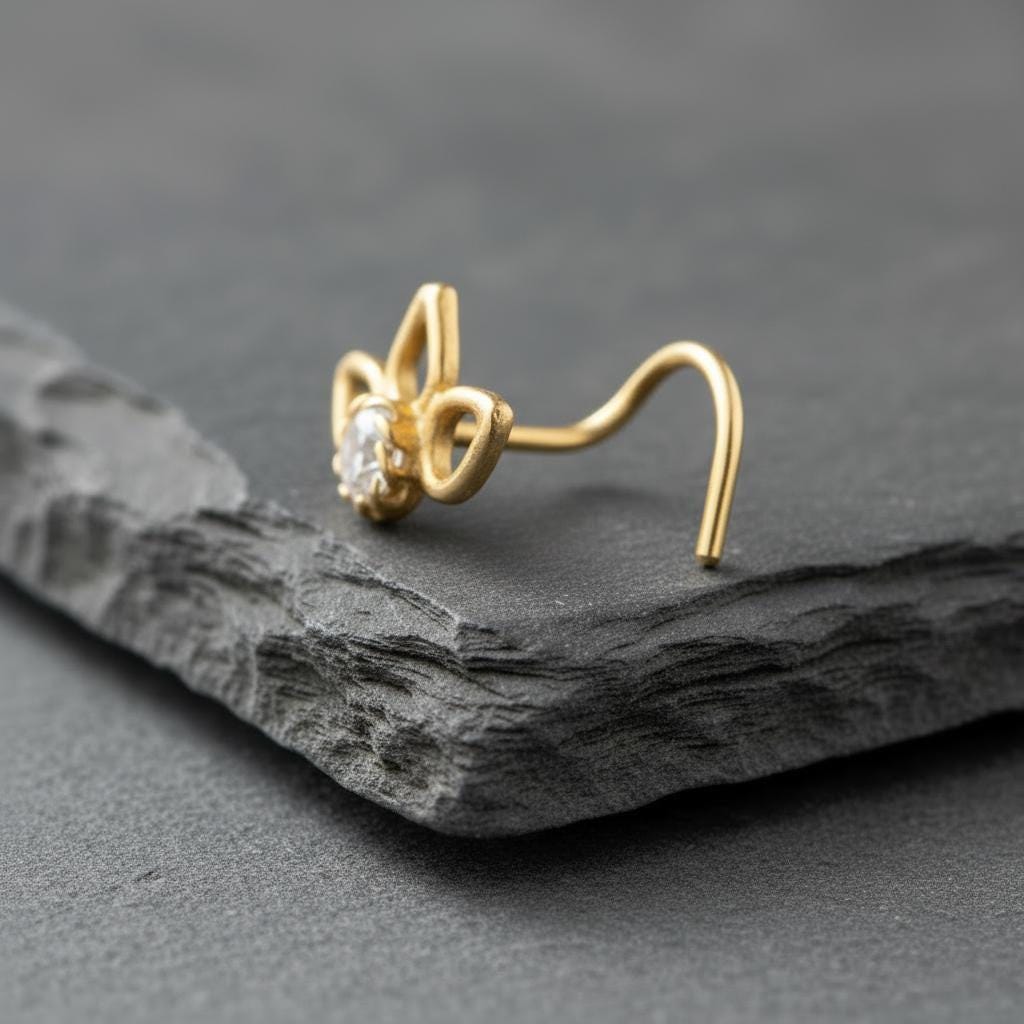 A gold-colored nose ring with a small gemstone is resting on a gray surface.